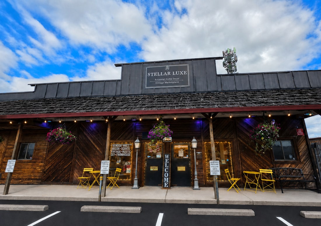 The Stellar Luxe storefront on Amboy Avenue in Yacolt, Washington, under a blue sky, with hanging baskets and yellow bistro chairs out front